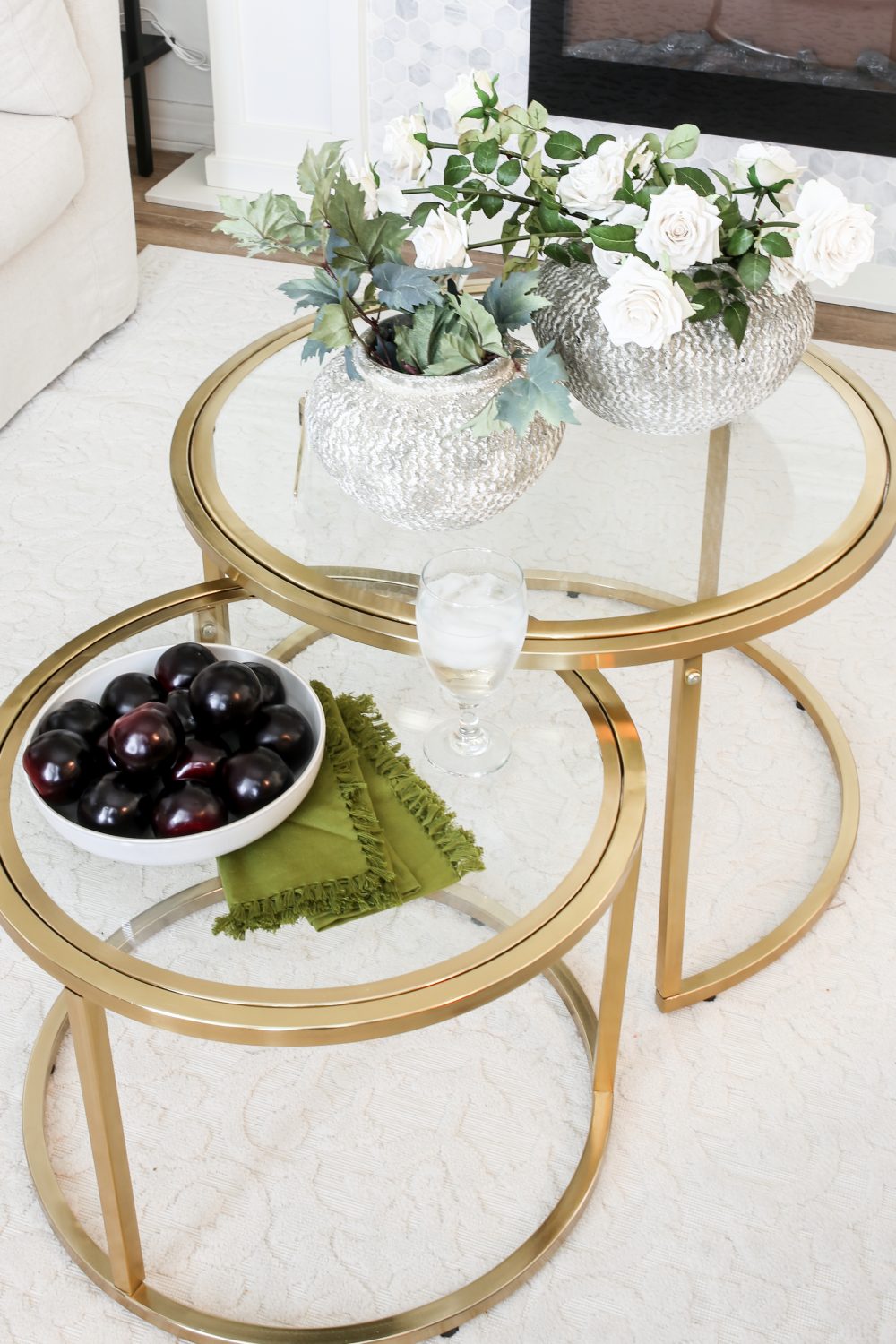 Gold Nesting Table with Flowers in a cement vase. There is also a bowl of plums. 