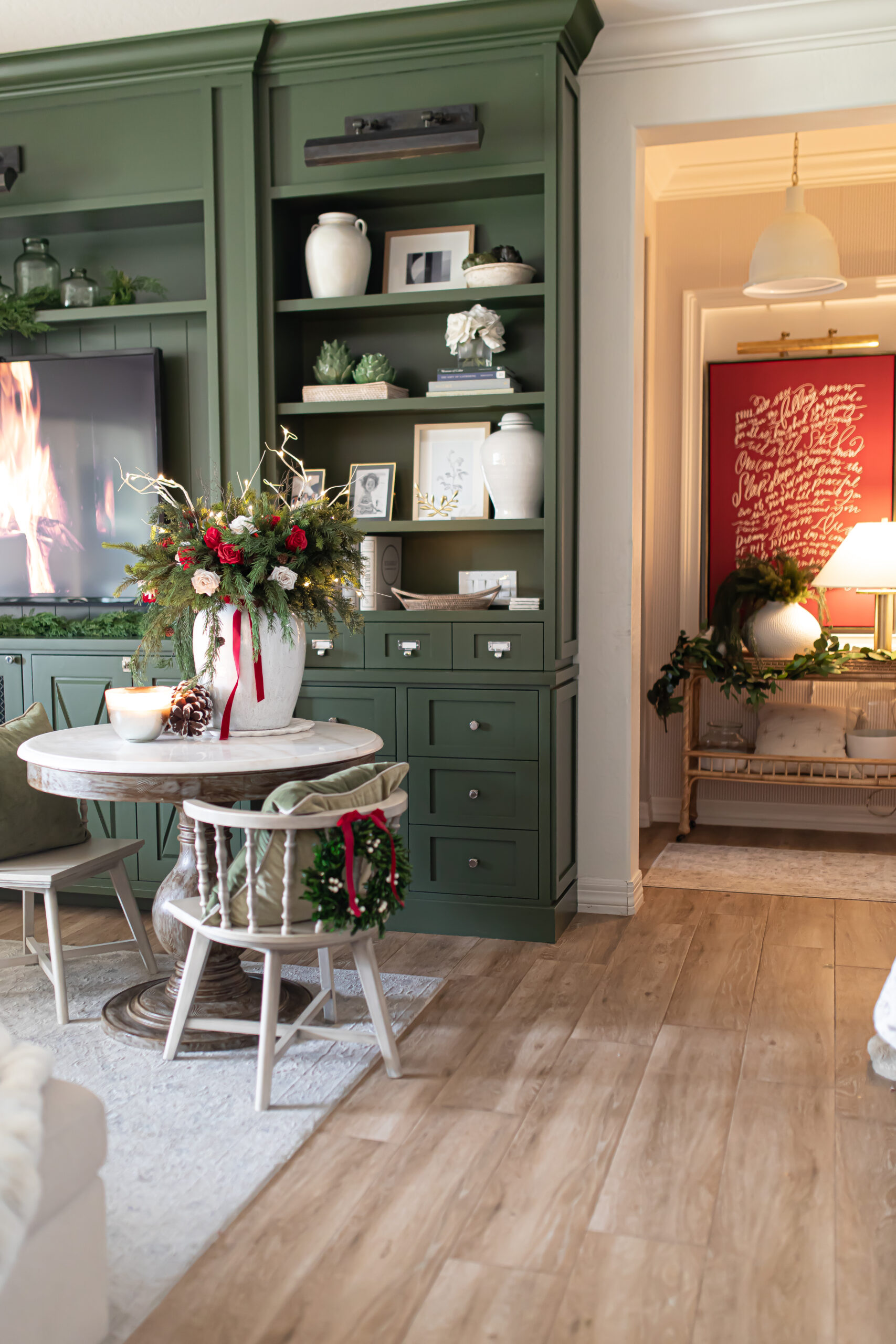 Christmas in the family room with red Christmas decor. A small chair and green bookcases are also in the shot. 