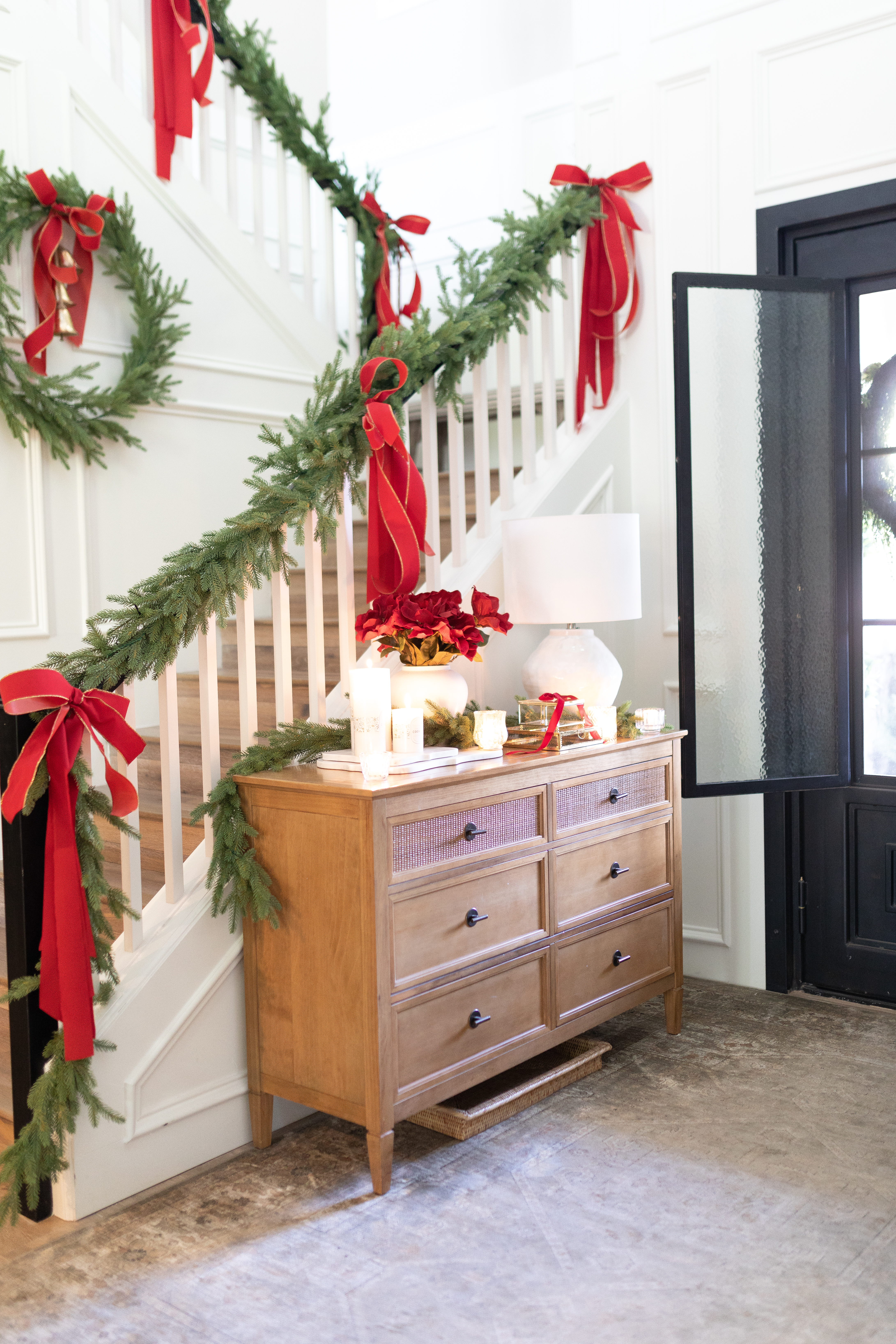 Red Christmas Decor in a festive entryway. Decorations are also green. THere is a black iron door with a neutral rug.