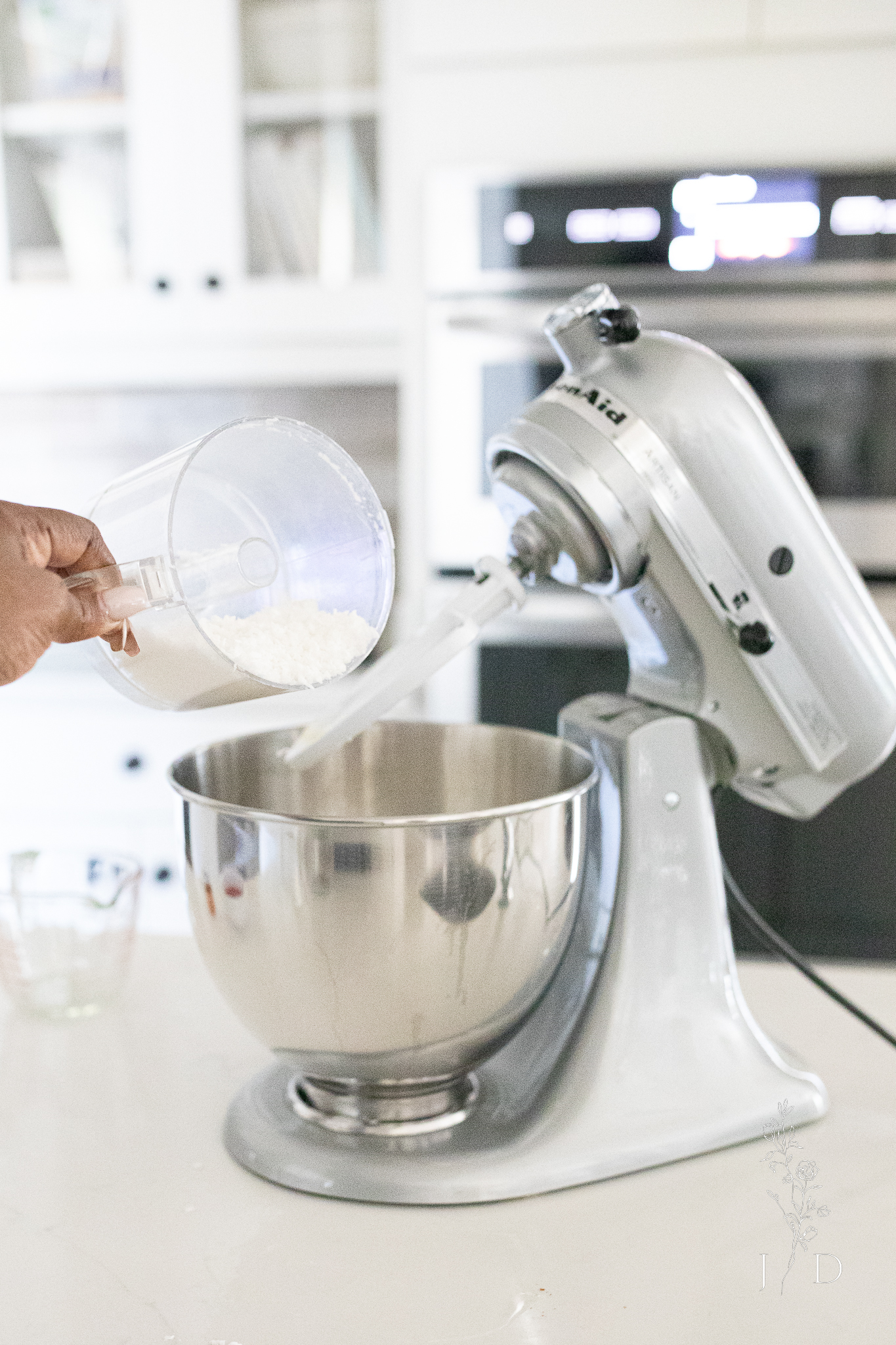 Coconut going into a cake mixer. Gray Stand Mixer from Kitchen aid in a white kitchen.